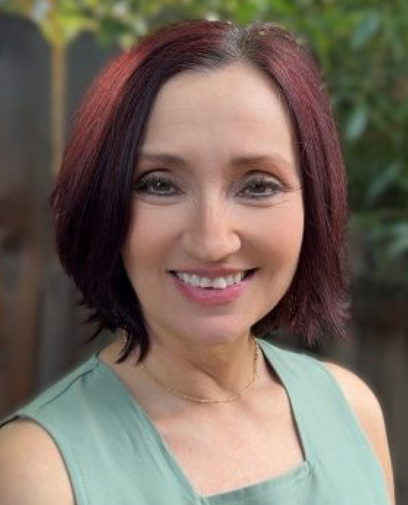 Smiling woman with short reddish-brown hair in a mint-green sleeveless top, outdoors.