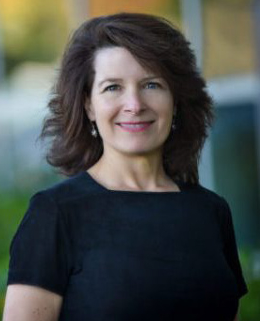 Professional headshot of a smiling woman with dark brown hair in a black top, outdoors setting