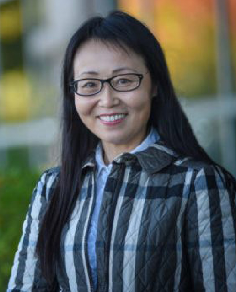 Smiling woman with long dark hair and glasses outdoors in a striped quilted jacket.